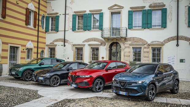 Mehrere Alfa Romeo Fahrzeuge in unterschiedlichen Farben stehen geparkt vor einem historischen Gebäude in einem Innenhof.