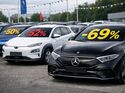 Mehrere gebrauchte Elektroautos stehen auf einem Parkplatz, auf den Frontscheiben sind prozentuale Wertverluste eingeblendet.