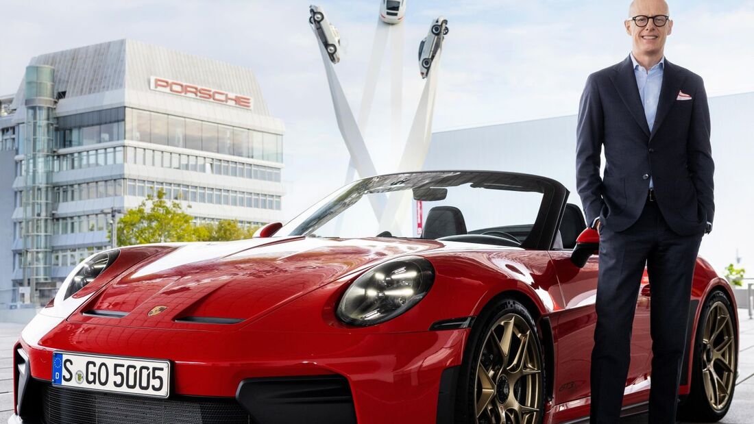 Michael Leiters steht neben einem roten Porsche 911 GT3 Cabriolet vor einem Porsche-Gebäude in Stuttgart.
