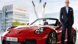 Michael Leiters steht neben einem roten Porsche 911 GT3 Cabriolet vor einem Porsche-Gebäude in Stuttgart.