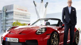 Michael Leiters steht neben einem roten Porsche 911 GT3 Cabriolet vor einem Porsche-Gebäude in Stuttgart.