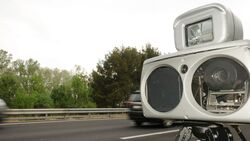 Mobiler Blitzer zur Geschwindigkeitsmessung am Straßenrand, vorbeifahrende Fahrzeuge unscharf, genutzt zur Darstellung von Messverfahren im Verkehrsrecht.