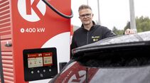 NAF-Vertreter steht neben einer Schnellladesäule und einem Elektroauto beim El Prix Ladetest. 