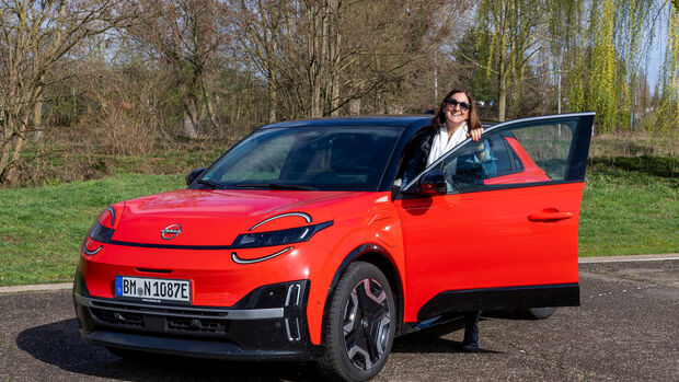 Nissan Micra mit geoeffneter Fahrertuer und Person neben dem Fahrzeug im Freien.