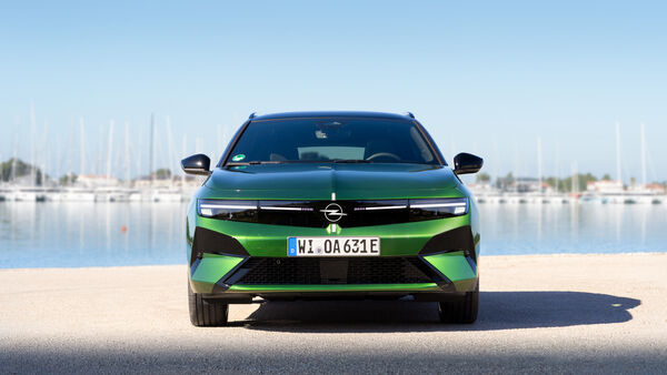 Opel Astra Electric in Grün frontal vor Hafenanlage mit Wasser im Hintergrund