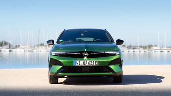 Opel Astra Electric in Grün frontal vor Hafenanlage mit Wasser im Hintergrund