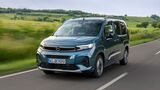 Opel Combo in blauer Lackierung während der Fahrt auf einer Landstraße vor ländlicher Landschaft.