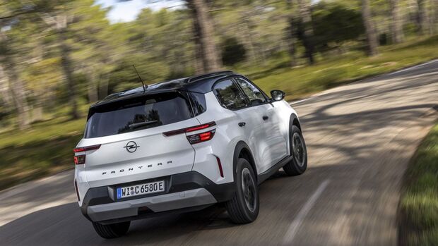 Opel Frontera Electric Extended Range in weiss, heckansicht schraeg, fahrend auf kurviger strasse im wald