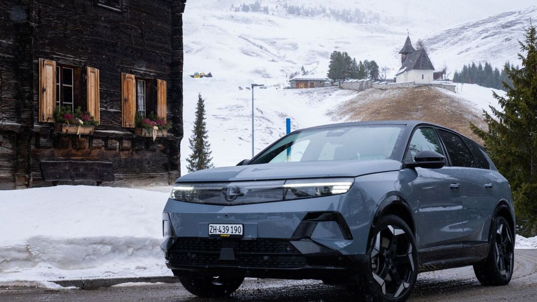 Opel Grandland Electric Ultimate AWD steht im Winter auf verschneiter Straße vor alpiner Landschaft mit Holzhäusern und Kapelle.