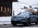 Opel Grandland Electric Ultimate AWD steht im Winter auf verschneiter Straße vor alpiner Landschaft mit Holzhäusern und Kapelle.