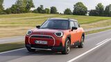 Orangefarbener Mini Aceman SE in Front-Dreiviertelansicht während der Fahrt auf einer Landstraße.