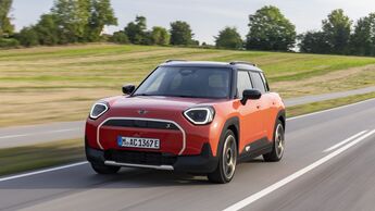Orangefarbener Mini Aceman SE in Front-Dreiviertelansicht während der Fahrt auf einer Landstraße.