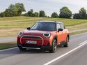 Orangefarbener Mini Aceman SE in Front-Dreiviertelansicht während der Fahrt auf einer Landstraße.