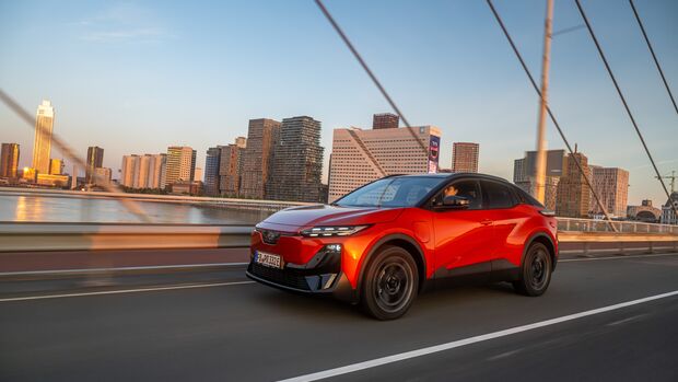 Orangefarbener Subaru Uncharted 77 FWD Active bei der Fahrt auf einer Brücke vor einer städtischen Kulisse.