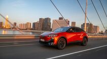 Orangefarbener Subaru Uncharted 77 FWD Active bei der Fahrt auf einer Brücke vor einer städtischen Kulisse.