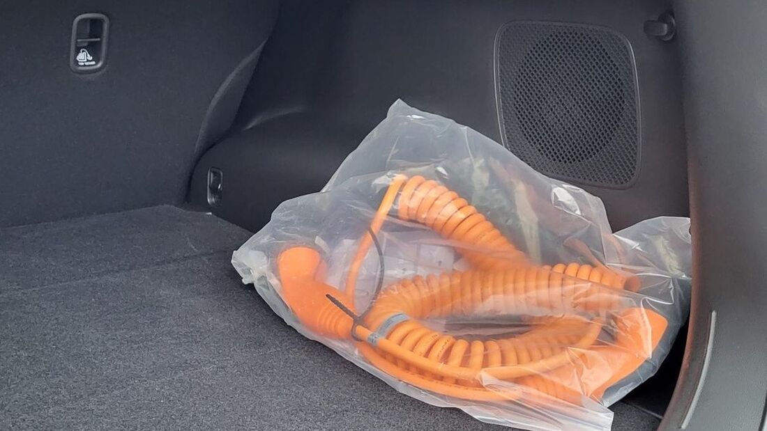 Oranges Ladekabel eines Plug-in-Hybrids liegt verpackt im Kofferraum eines Fahrzeugs.