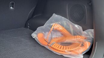Oranges Ladekabel eines Plug-in-Hybrids liegt verpackt im Kofferraum eines Fahrzeugs.