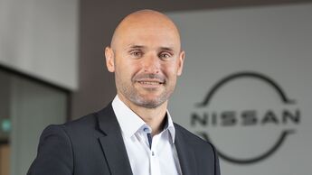 Pascal Michaeli von Nissan Deutschland steht in einem Bürogebäude vor einem Unternehmenslogo.