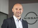 Pascal Michaeli von Nissan Deutschland steht in einem Bürogebäude vor einem Unternehmenslogo.