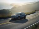Porsche Cayenne S Electric fährt auf einer kurvigen Küstenstraße bei Abendlicht.