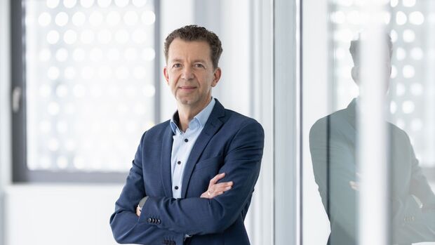 Portrait von Dr. Christian Dahlheim im Business-Outfit, stehend mit verschränkten Armen vor einer Glaswand in einem modernen Büro.