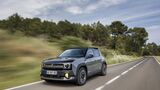 Renault 4 E-Tech Electric in grauer Lackierung während der Fahrt auf einer Landstraße mit bewaldeter Umgebung.