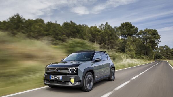 Renault 4 E-Tech Electric in grauer Lackierung während der Fahrt auf einer Landstraße mit bewaldeter Umgebung.