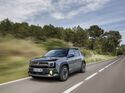 Renault 4 E-Tech Electric in grauer Lackierung während der Fahrt auf einer Landstraße mit bewaldeter Umgebung.