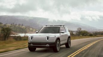 Rivian R2 in heller Lackierung auf einer Landstraße mit Berglandschaft im Hintergrund.