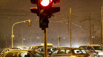Rot zeigende Ampel an einer innerstädtischen Kreuzung bei starkem Verkehr und schlechten Sichtverhältnissen in der Dämmerung