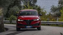 Roter Alfa Romeo Tonale in Fahrt, Frontansicht auf kurviger Straße mit Leitplanke und Bäumen im Hintergrund.