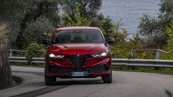 Roter Alfa Romeo Tonale in Fahrt, Frontansicht auf kurviger Straße mit Leitplanke und Bäumen im Hintergrund.