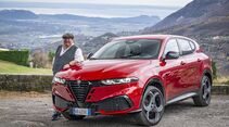 Roter Alfa Romeo Tonale in schräger Frontansicht, eine Person steht neben dem Fahrzeug, Landschaft und Tal im Hintergrund.