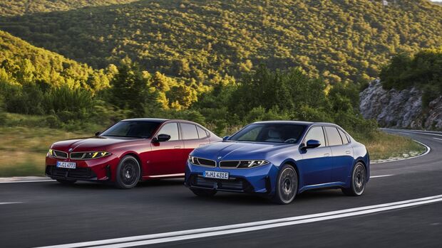 Roter BMW 3er und blauer BMW i3 fahren nebeneinander auf einer Straße durch eine bewaldete Berglandschaft.