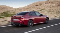Roter BMW M350 xDrive in Heck-Seiten-Ansicht während der Fahrt auf einer Straße durch eine felsige Landschaft.