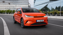 Roter BYD DOLPHIN G DM-i fährt auf einer urbanen Straße vor moderner Glasfassade.