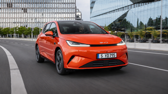 Roter BYD DOLPHIN G DM-i fährt auf einer urbanen Straße vor moderner Glasfassade.