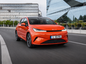 Roter BYD DOLPHIN G DM-i fährt auf einer urbanen Straße vor moderner Glasfassade.