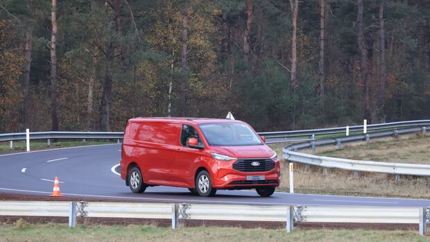 Roter Ford Transit Custom fährt auf einer Teststrecke beim Ford Pro Leisure Experience Event in Lommel, mit Leitplanken und Pylonen.
