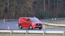 Roter Ford Transit Custom fährt auf einer Teststrecke beim Ford Pro Leisure Experience Event in Lommel, mit Leitplanken und Pylonen.