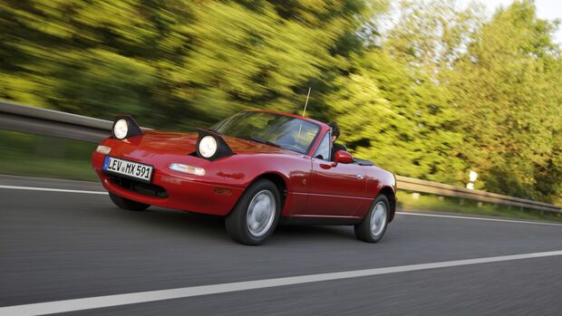 Roter Mazda MX-5 der ersten Generation NA mit geöffneten Klappscheinwerfern während der Fahrt.