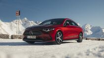 Roter Mercedes CLA in Seitenansicht auf verschneiter Passfläche, Berge und blauer Himmel im Hintergrund.