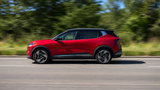 Roter Mitsubishi Eclipse Cross Elektro-SUV fährt auf einer Landstraße vor grünem Hintergrund.