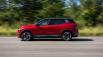 Roter Mitsubishi Eclipse Cross Elektro-SUV fährt auf einer Landstraße vor grünem Hintergrund.