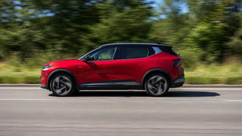 Roter Mitsubishi Eclipse Cross Elektro-SUV fährt auf einer Landstraße vor grünem Hintergrund.