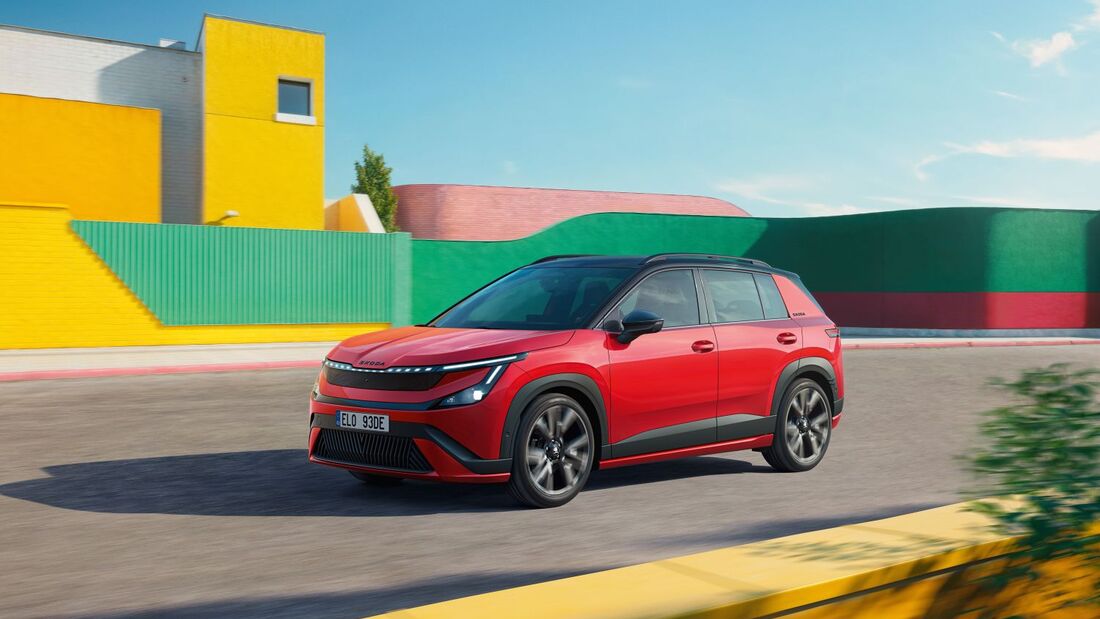 Roter Skoda Epiq Sportline mit schwarzem Dach und großen Leichtmetallrädern fährt auf einer Straße vor gelben und grünen Gebäudefassaden.