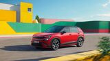 Roter Skoda Epiq Sportline mit schwarzem Dach und großen Leichtmetallrädern fährt auf einer Straße vor gelben und grünen Gebäudefassaden.