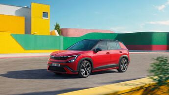 Roter Skoda Epiq Sportline mit schwarzem Dach und großen Leichtmetallrädern fährt auf einer Straße vor gelben und grünen Gebäudefassaden.