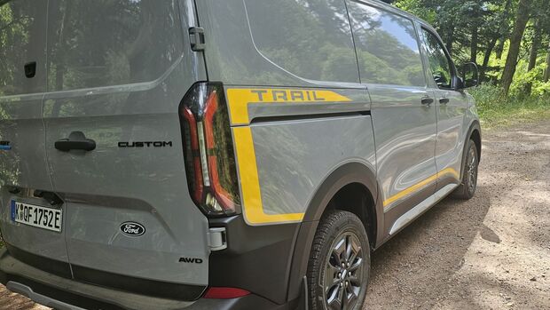 Schräg von hinten fotografierter Ford E-Transit Custom AWD Trail mit gelben Trail-Designelementen.