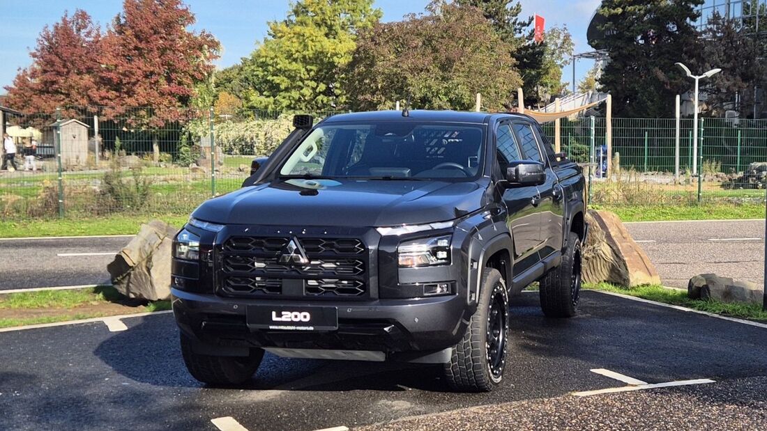 Schwarzer Mitsubishi L200 mit Offroad-Bereifung, Schnorchel und schwarzem Kühlergrill in schräger Frontansicht auf einem Parkplatz.